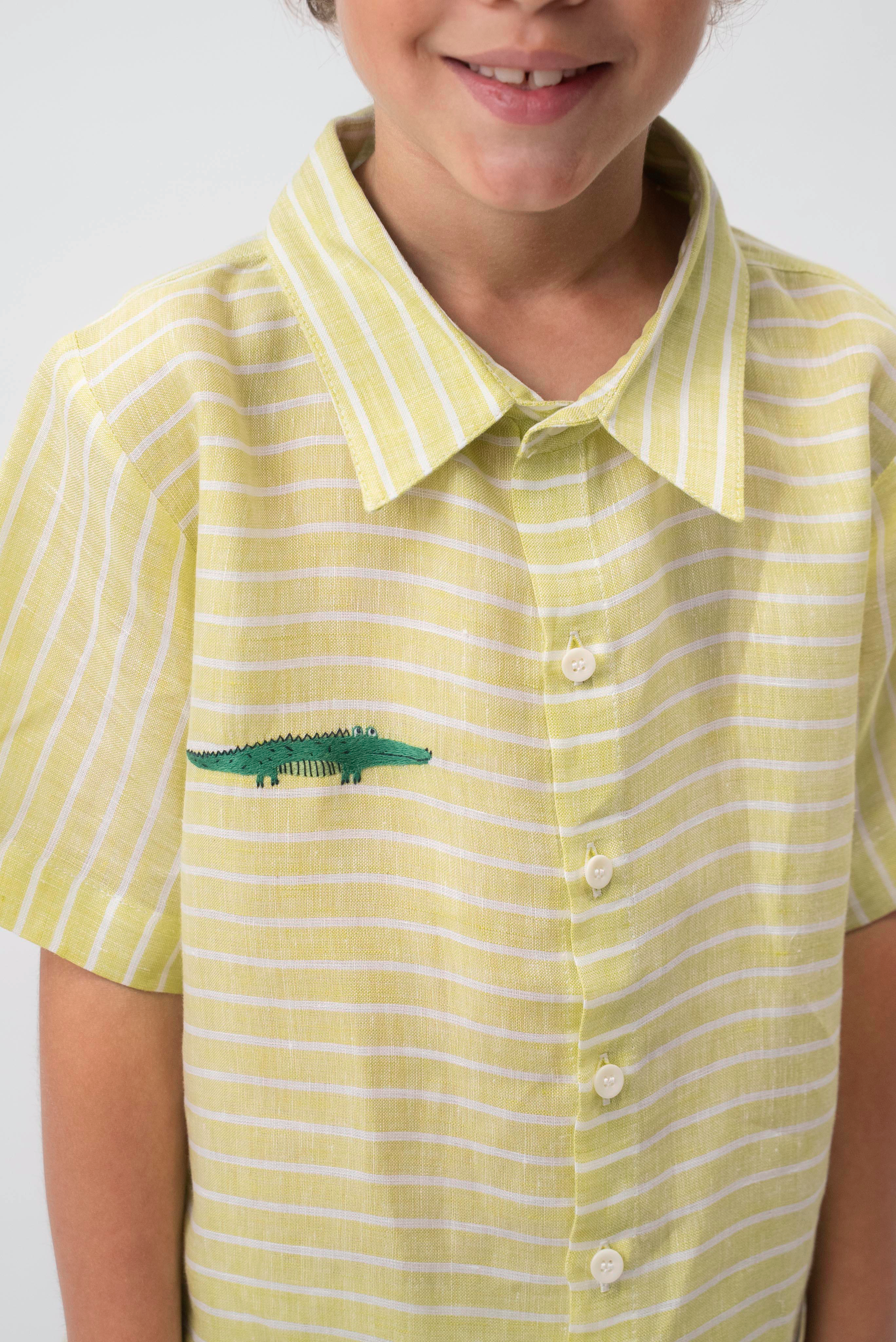 Detalhe da Camisa Tom em linho verde listrado vestida, com gola clássica, botões claros e jacaré bordado à mão.