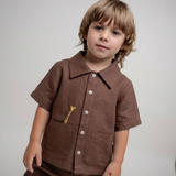 Menino vestindo camisa infantil de linho marrom com bordado à mão de girafa no bolso.