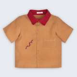 Camisa Luca infantil em 100% linho caramelo com gola vermelha, bolso frontal e cobra-coral bordada à mão, vista frontal.