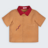 Camisa Luca infantil em 100% linho caramelo com gola vermelha, bolso frontal e cobra-coral bordada à mão, vista frontal.