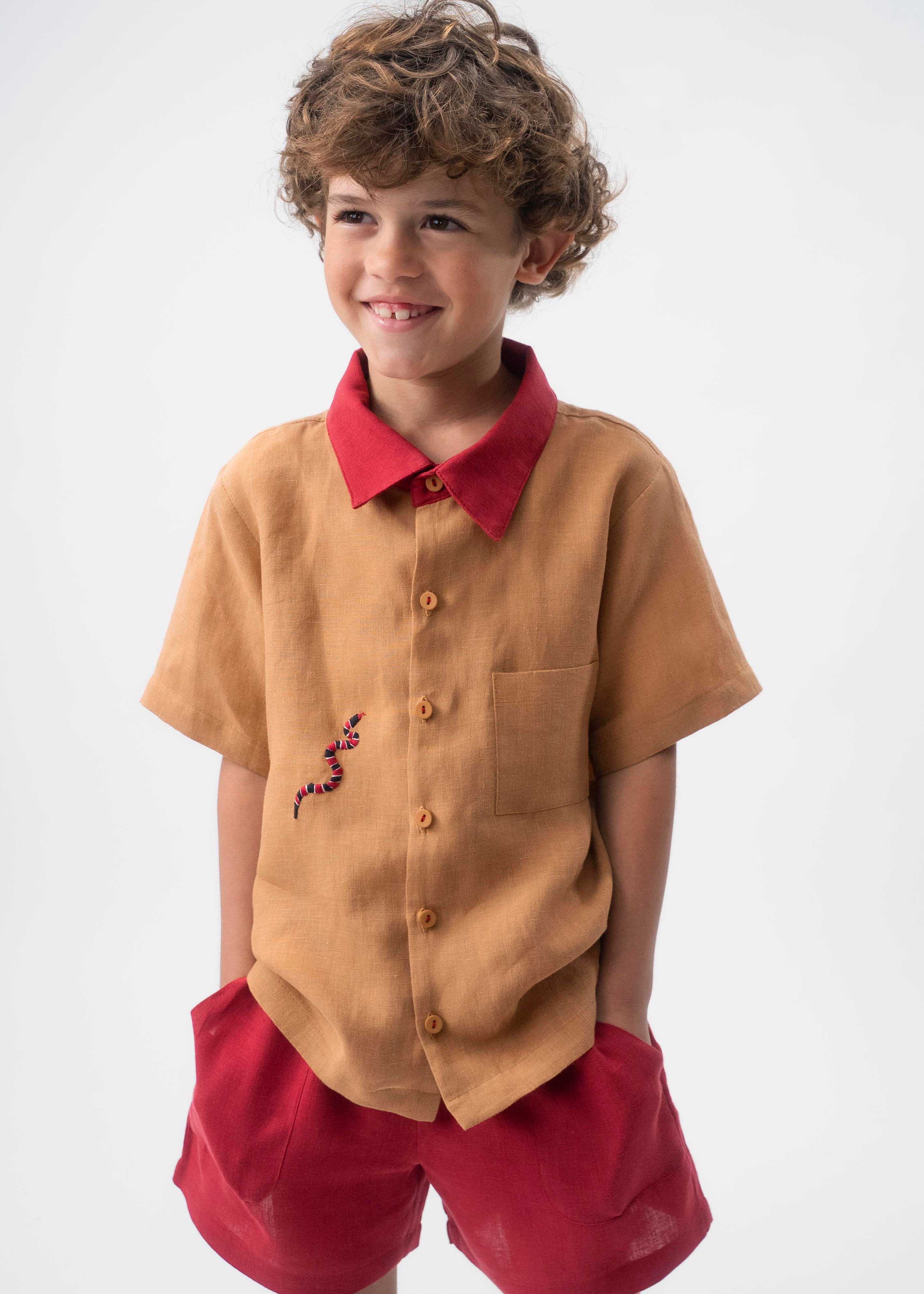 Detalhe da Camisa Luca infantil em linho caramelo vestida, com gola vermelha, bolso frontal e bordado de cobra-coral.