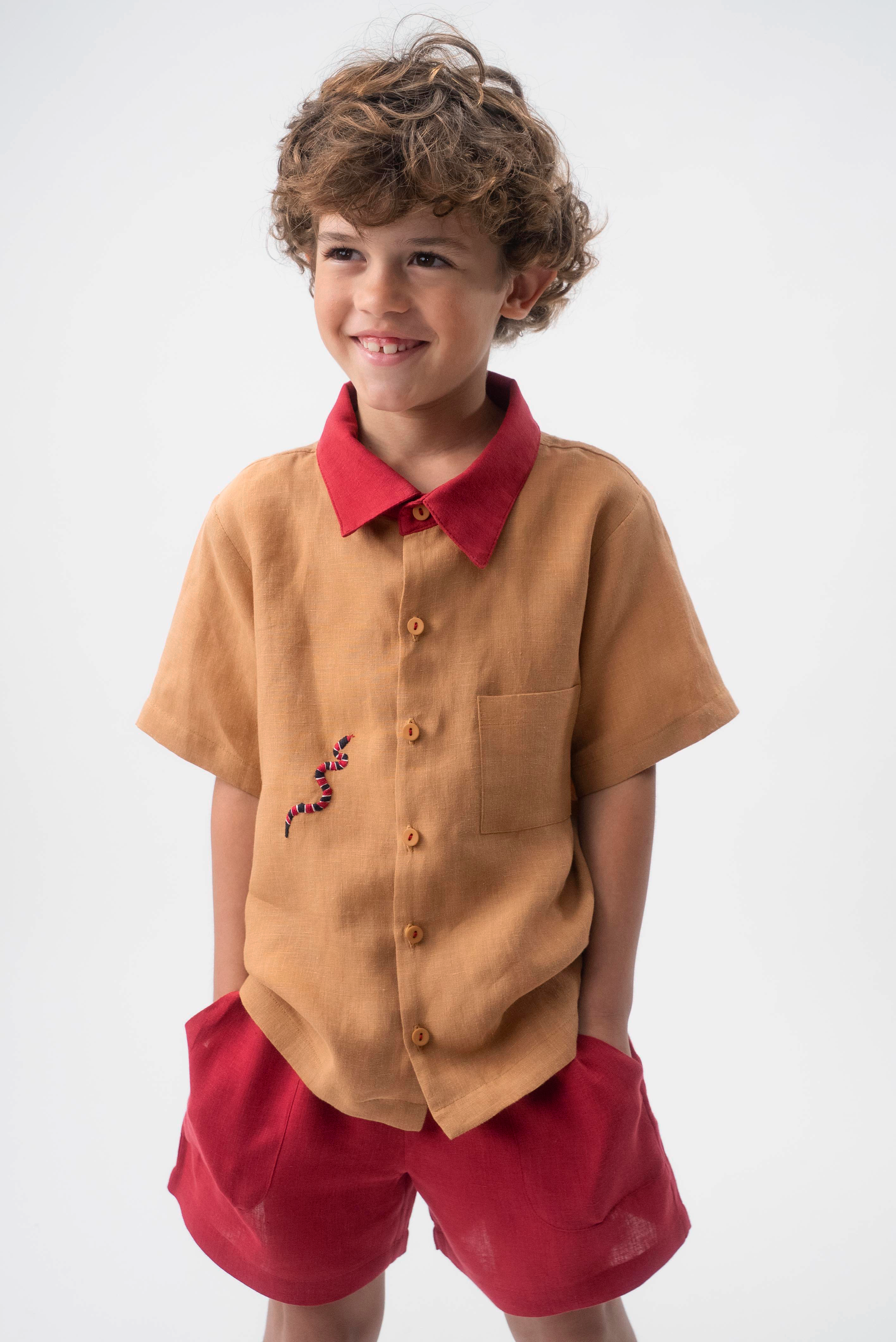 Detalhe da Camisa Luca infantil em linho caramelo vestida, com gola vermelha, bolso frontal e bordado de cobra-coral.