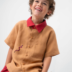 Menino sentado usando Camisa Luca em linho caramelo com gola vermelha contrastante e cobra-coral bordada à mão.