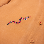 Detalhe da Camisa Luca infantil em linho caramelo com cobra-coral bordada à mão e botões com linha vermelha.