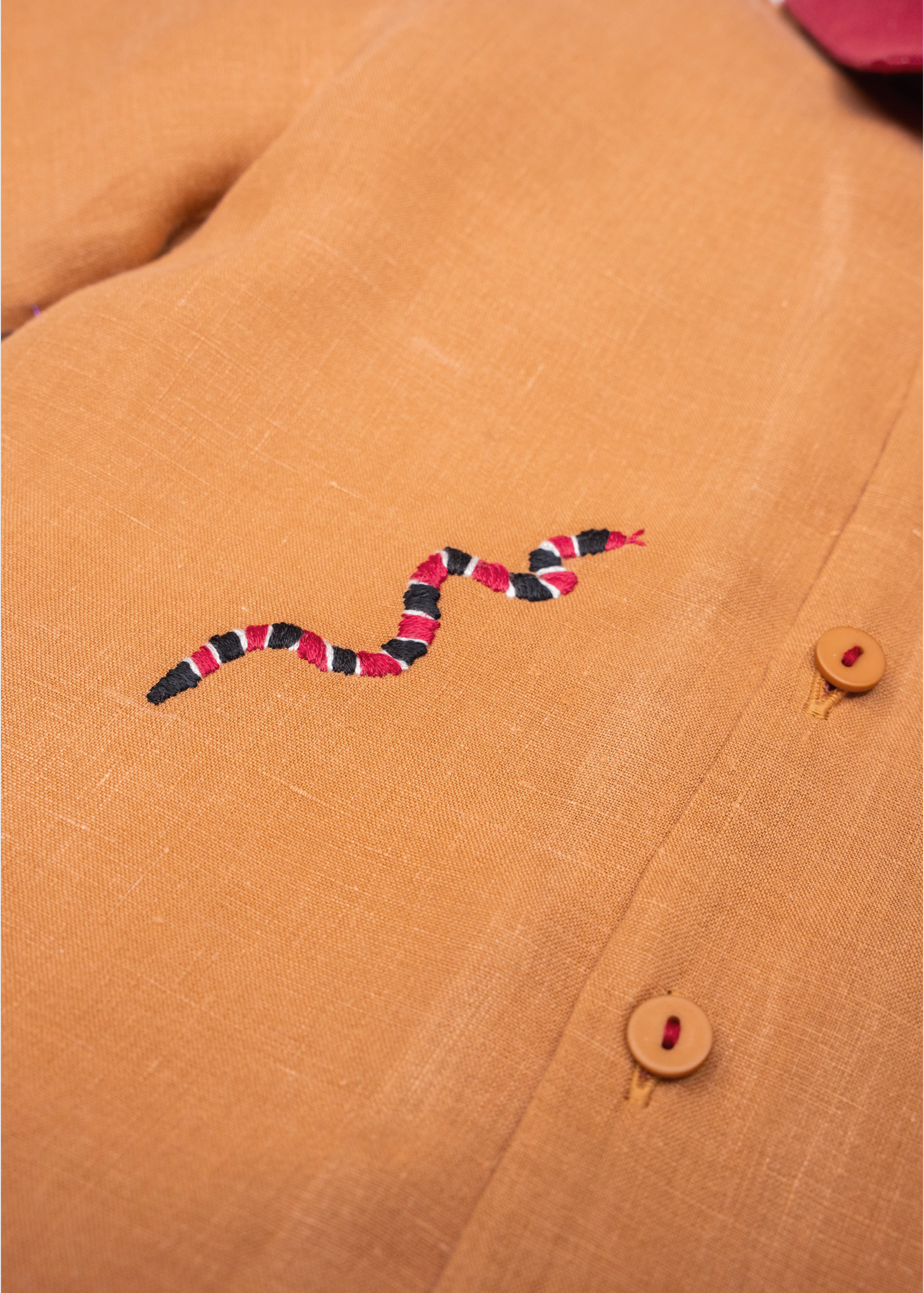 Detalhe da Camisa Luca infantil em linho caramelo com cobra-coral bordada à mão e botões com linha vermelha.