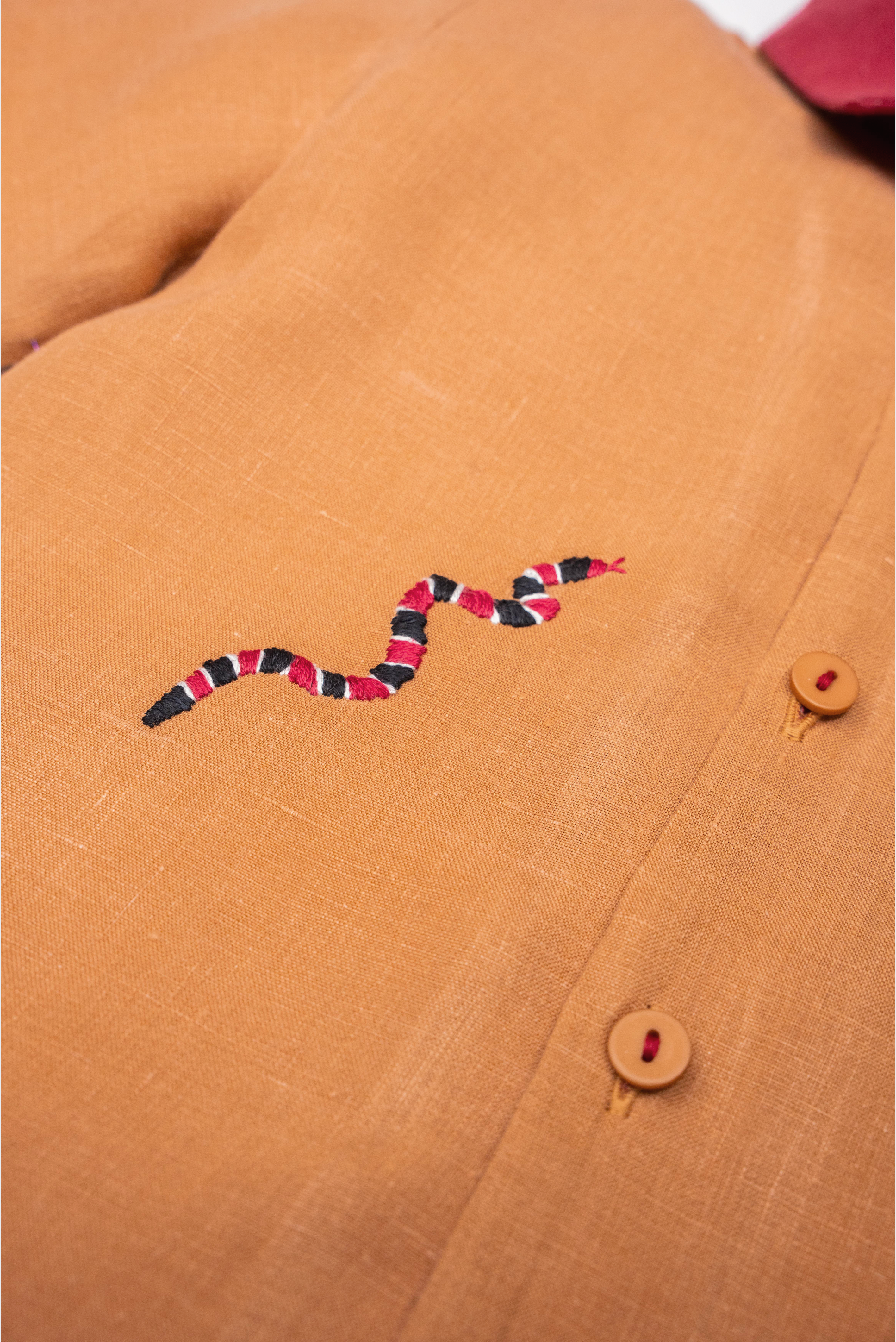 Detalhe da Camisa Luca infantil em linho caramelo com cobra-coral bordada à mão e botões com linha vermelha.