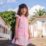 Menina sorrindo usando camisa infantil em linho rosa com mangas de babado listrado e bordado de sorvete de casquinha no peito, combinando com uma saia listrada.