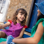 Menina usando camisa infantil em linho roxo com mangas com babado vermelho e bordado de bichinhos do fundo do mar entre os botões.
