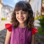 Menina sorrindo usando camisa infantil em linho roxo com mangas de babado vermelho e bordado de bichinhos do fundo do mar entre os botões.