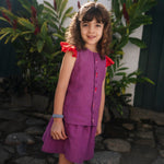Menina usando camisa infantil em linho roxo com mangas de babado vermelho e bordado de bichinhos do fundo do mar entre os botões, com saia combinando.