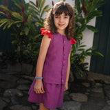 Menina usando camisa infantil em linho roxo com mangas de babado vermelho e bordado de bichinhos do fundo do mar entre os botões, com saia combinando.