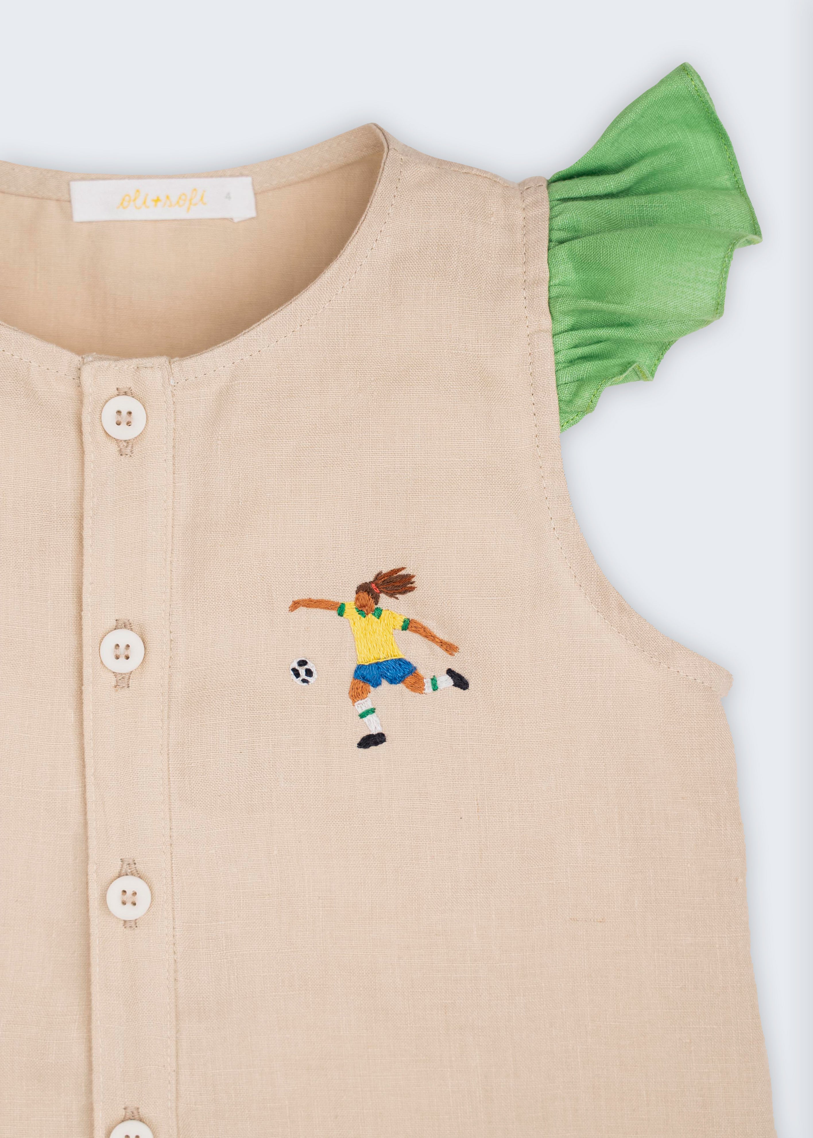 Detalhe de camisa infantil em linho puro com bordado à mão de jogadora de futebol e mangas de babados verde 