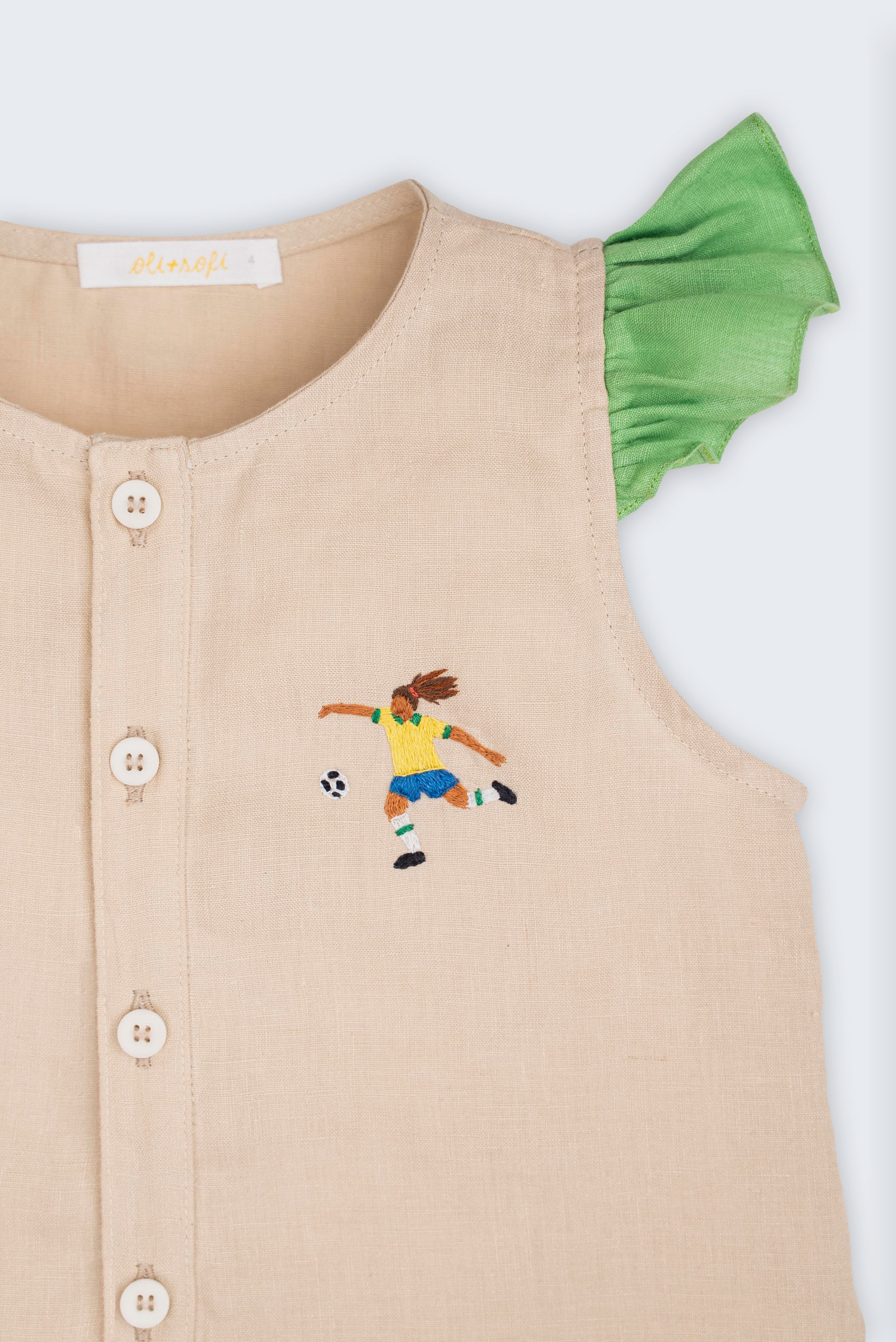 Detalhe de camisa infantil em linho puro com bordado à mão de jogadora de futebol e mangas de babados verde 