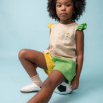 Menina usando camisa infantil em linho com bordado de jogadora de futebol, combinada com shorts verde e amarelo