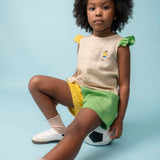 Menina usando camisa infantil em linho com bordado de jogadora de futebol, combinada com shorts verde e amarelo