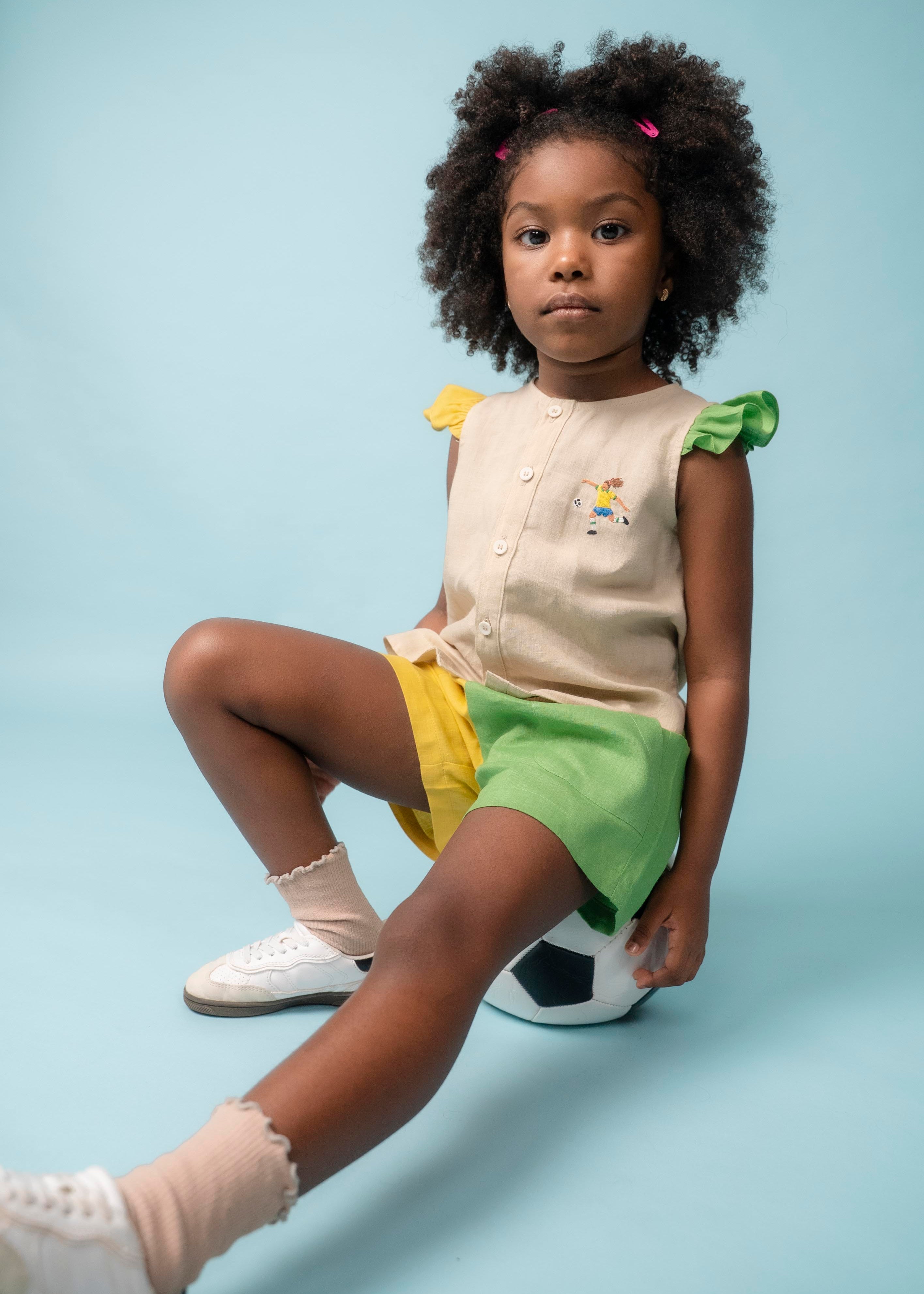 Menina usando camisa infantil em linho com bordado de jogadora de futebol, combinada com shorts verde e amarelo