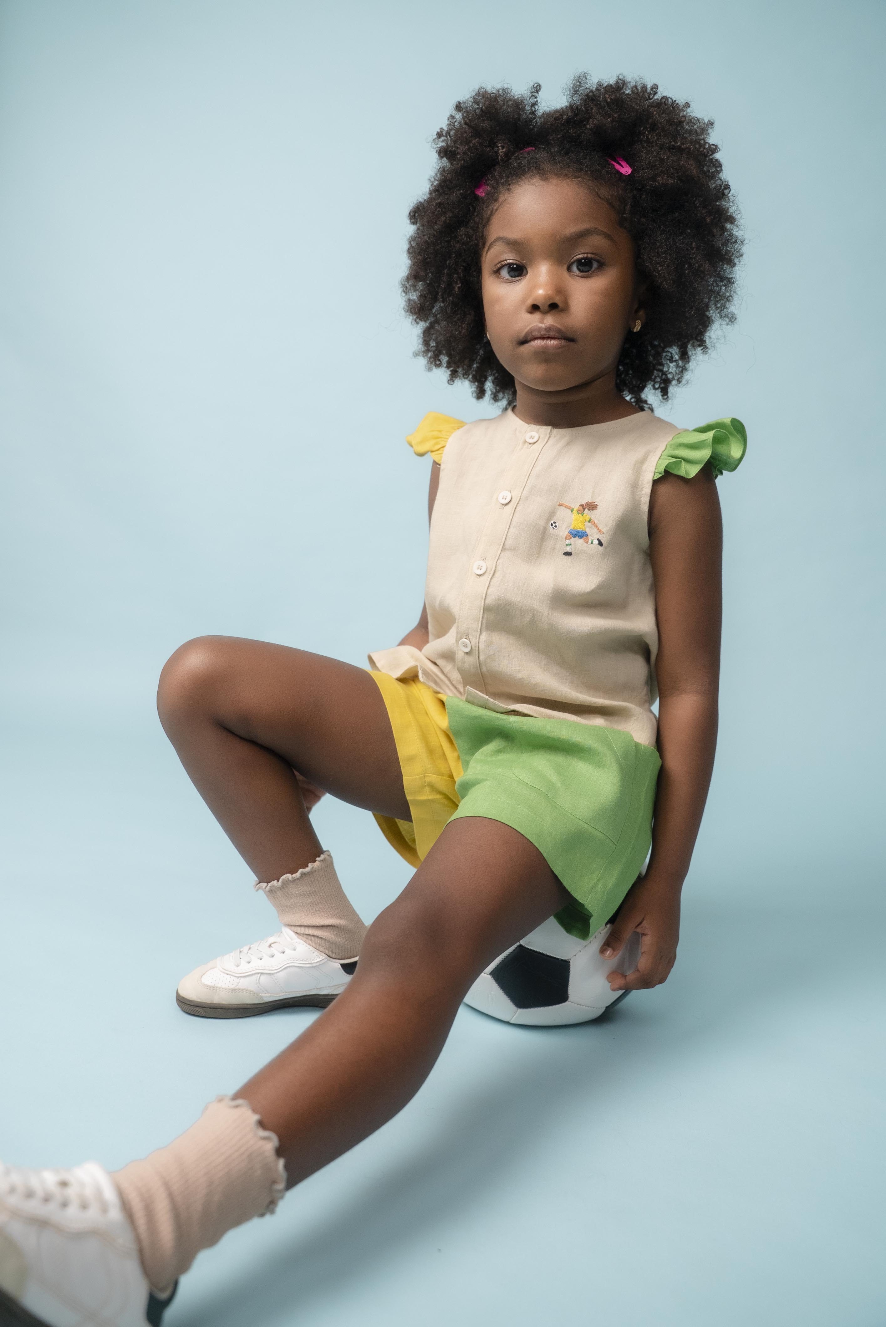 Menina usando camisa infantil em linho com bordado de jogadora de futebol, combinada com shorts verde e amarelo