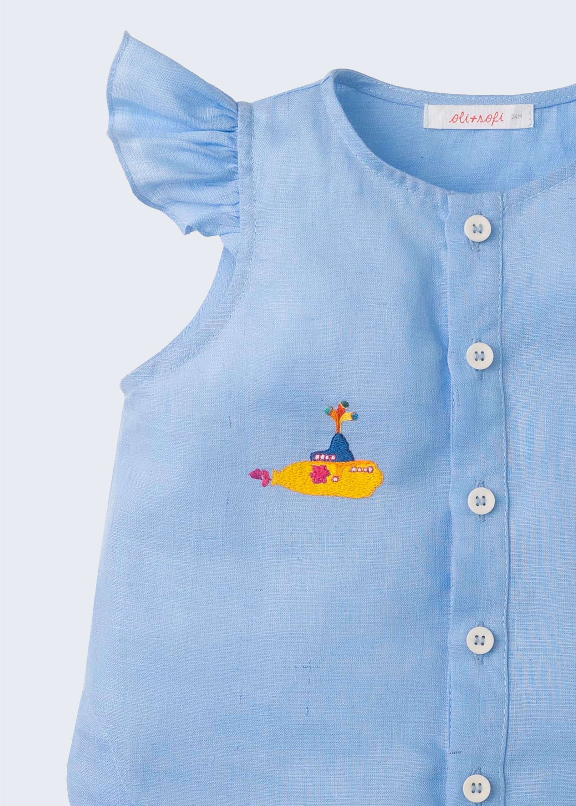 Close de camisa azul infantil em linho com botões brancos frontais e manga de babado, bordada à mão com submarino amarelo dos Beatles.