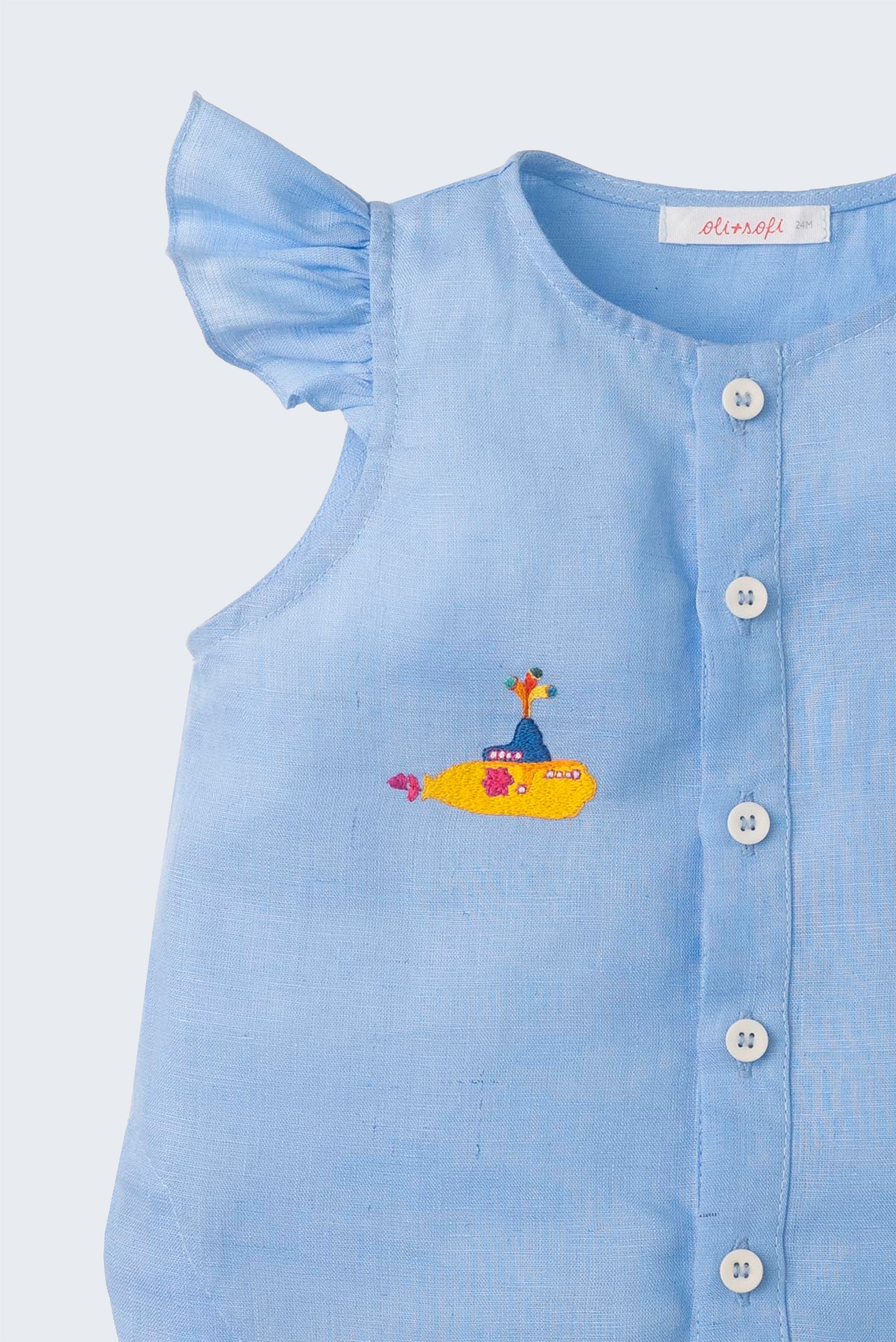 Close de camisa azul infantil em linho com botões brancos frontais e manga de babado, bordada à mão com submarino amarelo dos Beatles.