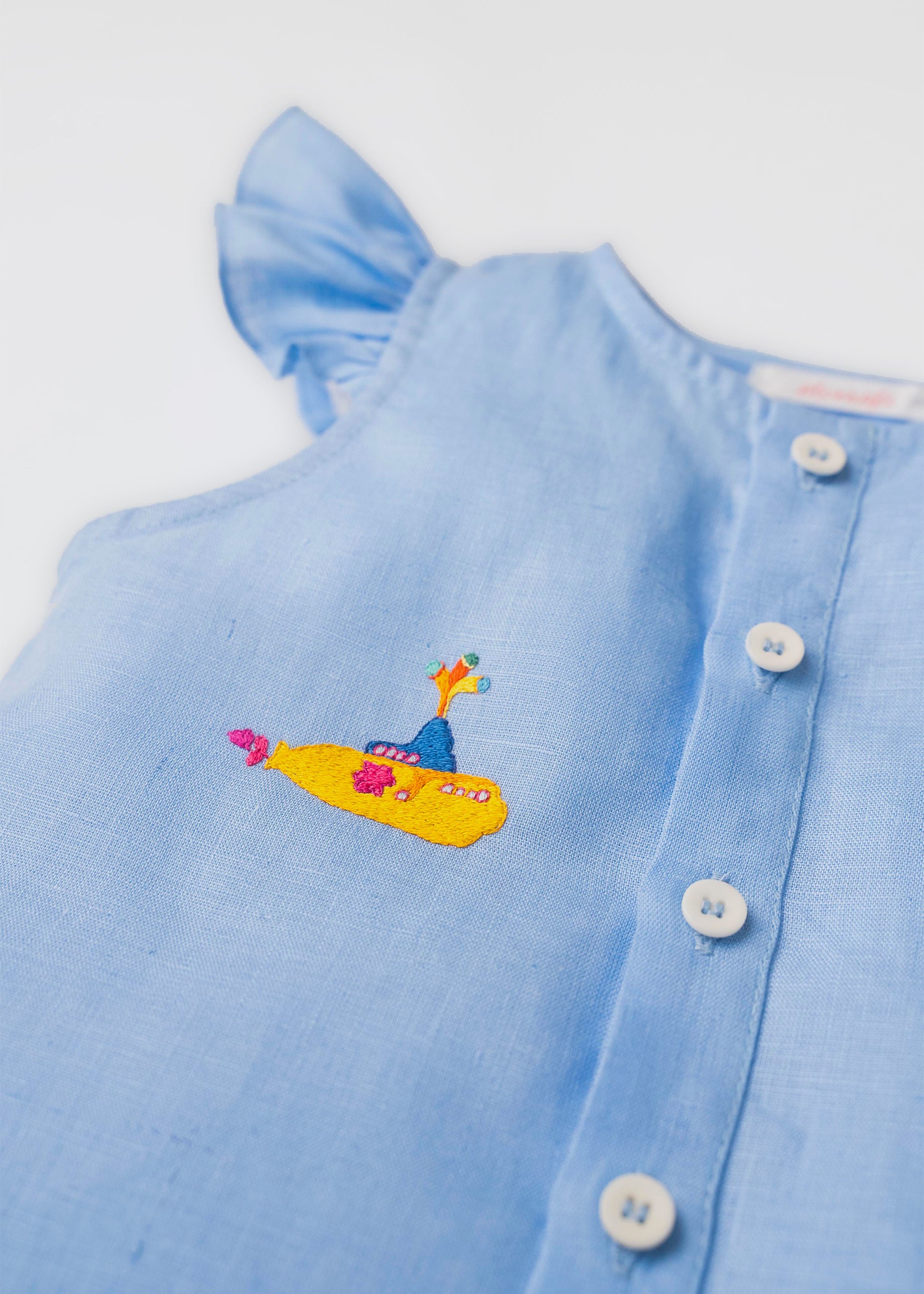 Detalhe do bordado manual de submarino amarelo inspirado em Yellow Submarine, dos Beatles, em camisa azul infantil de linho.