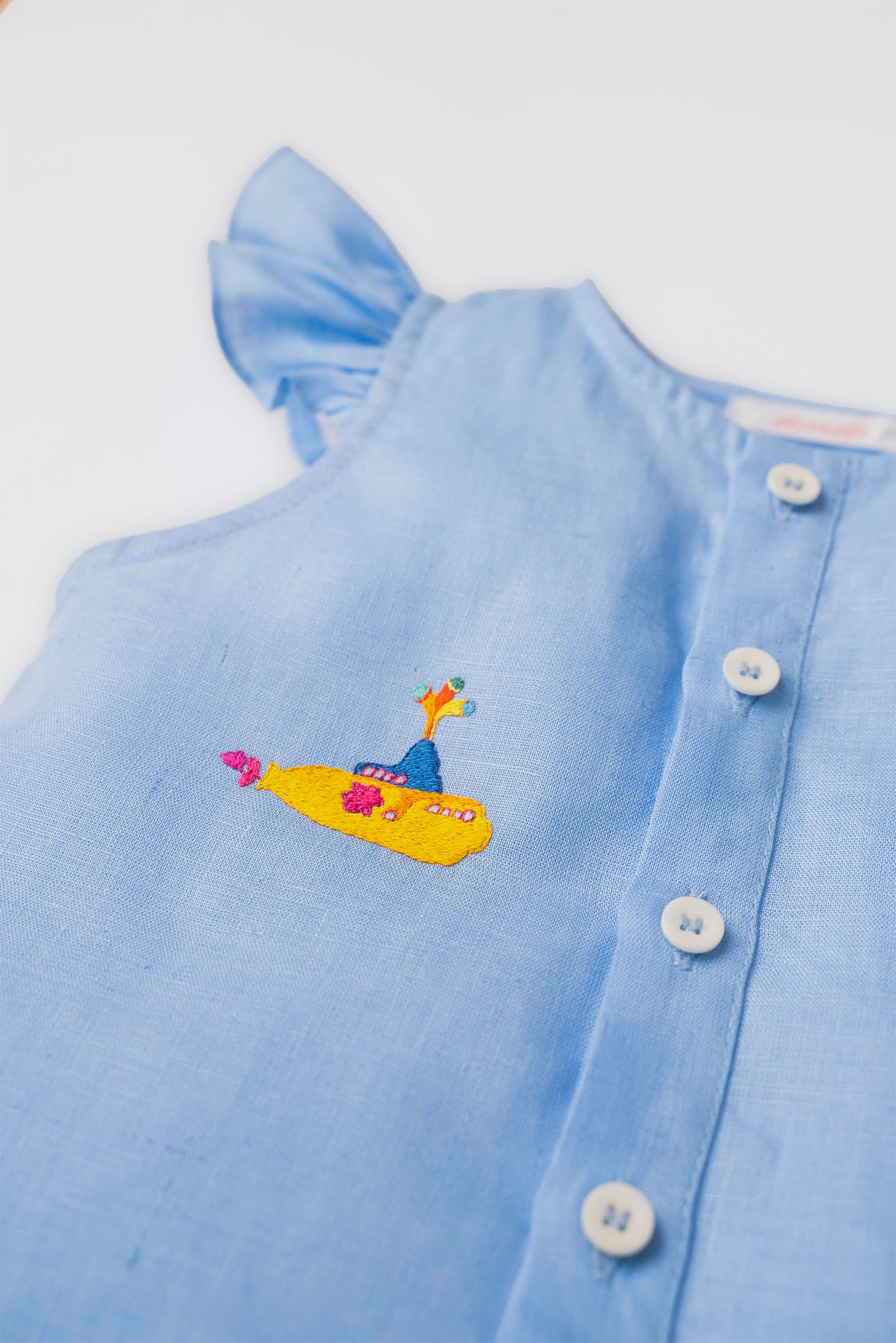 Detalhe do bordado manual de submarino amarelo inspirado em Yellow Submarine, dos Beatles, em camisa azul infantil de linho.