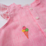 Detalhe do bordado à mão de sorvete de casquinha no peito da camisa infantil menina em linho rosa com mangas de babado listrado.