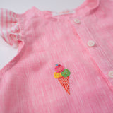 Detalhe do bordado à mão de sorvete de casquinha no peito da camisa infantil menina em linho rosa com mangas de babado listrado.