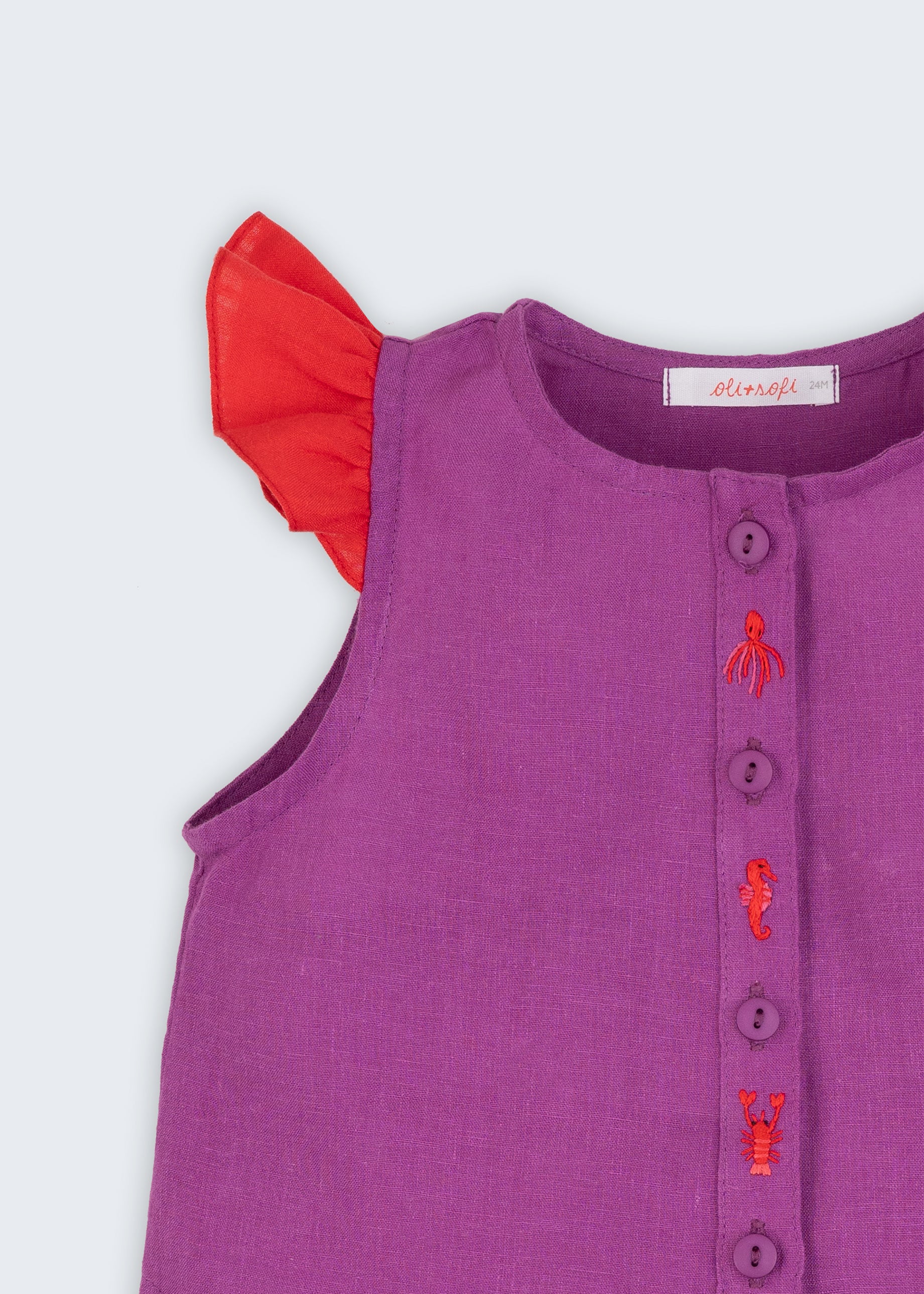 Camisa infantil menina em linho roxo com mangas de babado vermelho e bordado de bichinhos do fundo do mar entre os botões, vista de frente em detalhe.