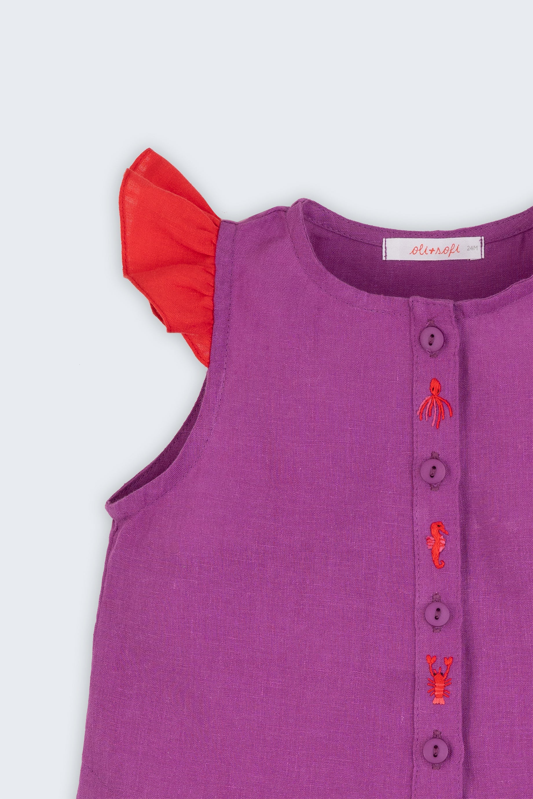Camisa infantil menina em linho roxo com mangas de babado vermelho e bordado de bichinhos do fundo do mar entre os botões, vista de frente em detalhe.