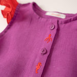 Detalhe dos bordados à mão de polvo e cavalo marinho da camisa infantil menina em linho roxo com mangas de babado vermelho vibrante.