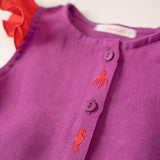 Detalhe dos bordados à mão de polvo e cavalo marinho da camisa infantil menina em linho roxo com mangas de babado vermelho vibrante.