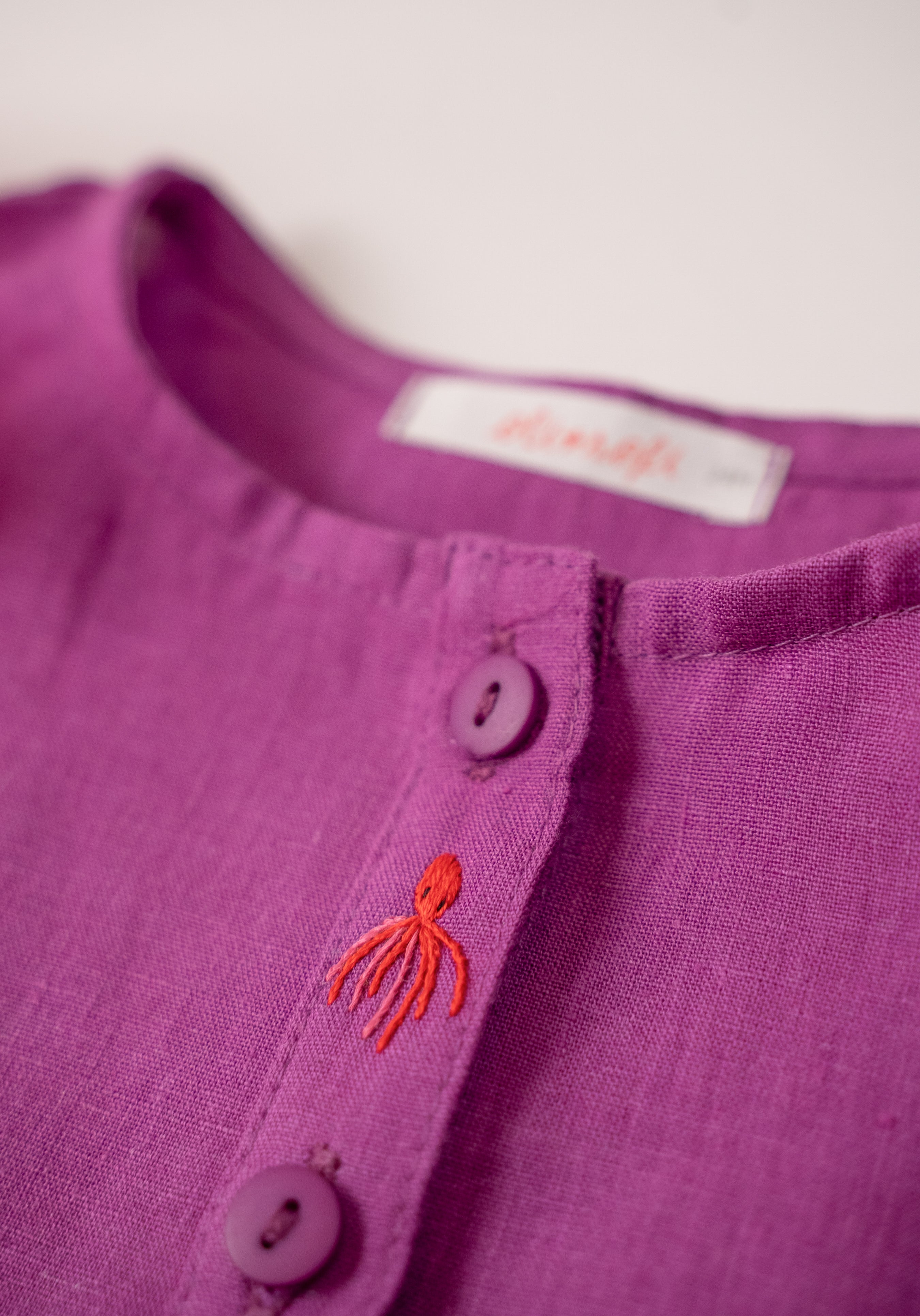 Detalhe do bordado à mão de polvo e da camisa infantil menina em linho roxo com bordados de bichinhos do fundo do mar.