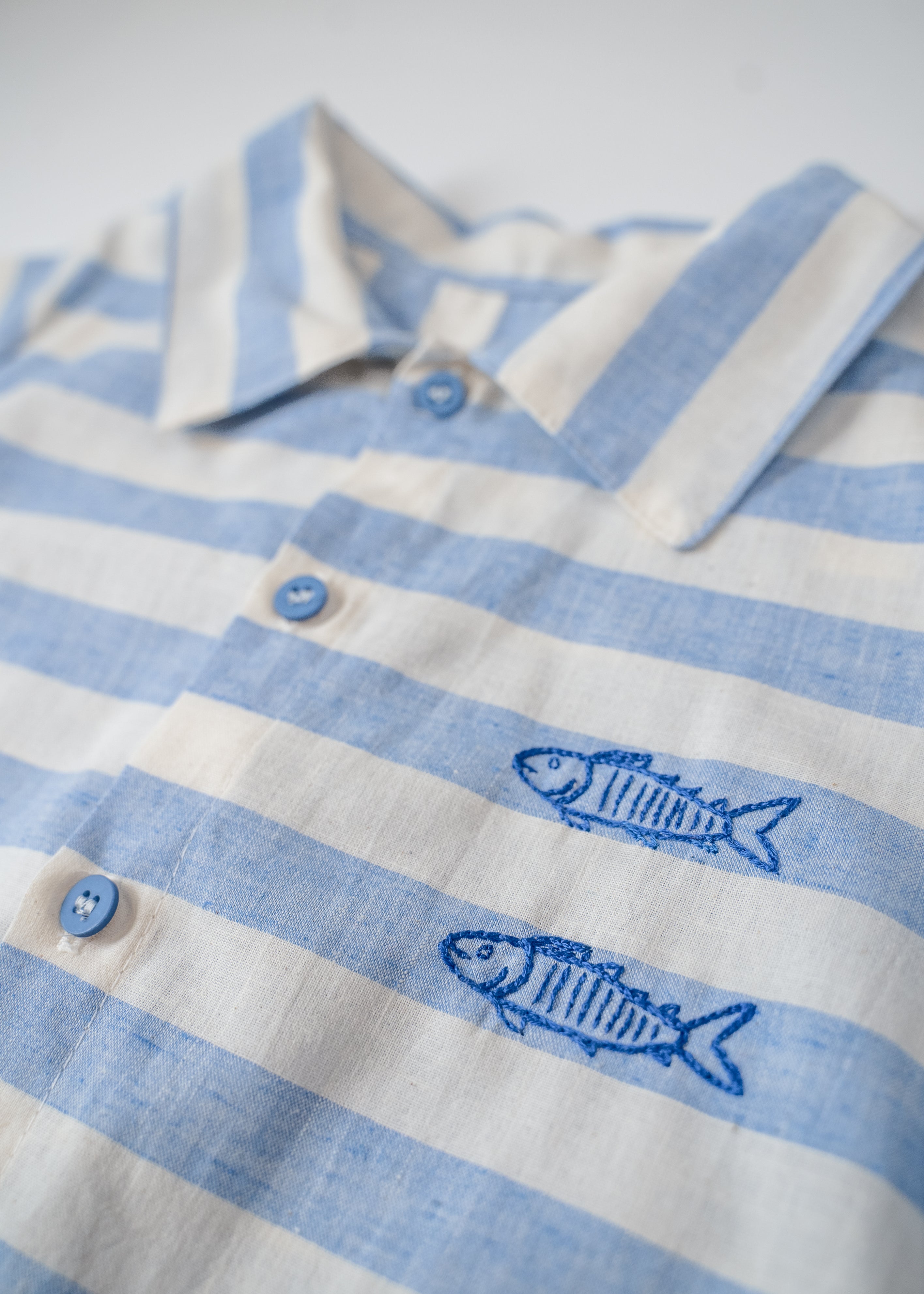 Detalhe dos peixes bordados à mão nas listras azuis da camisa infantil.