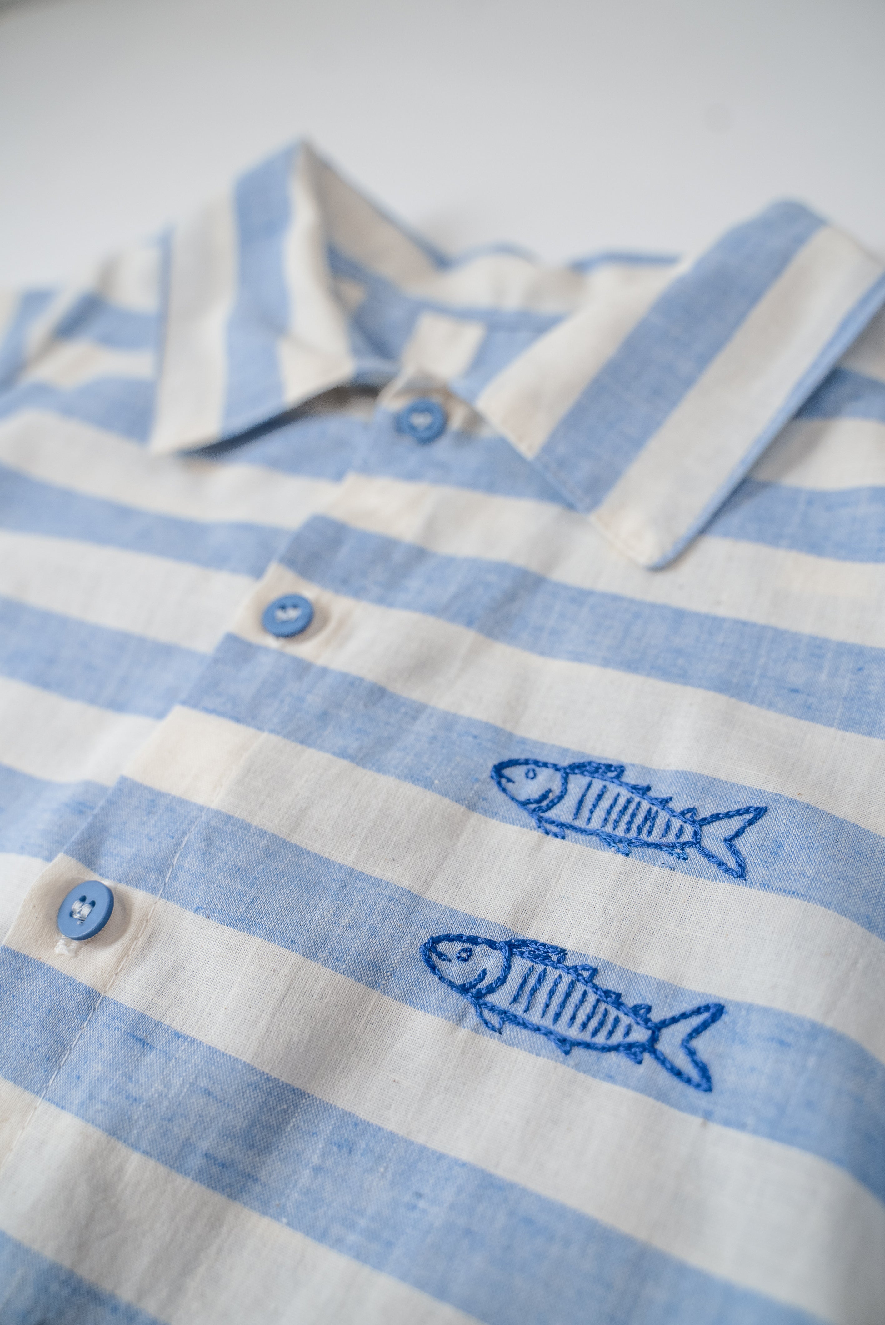 Detalhe dos peixes bordados à mão nas listras azuis da camisa infantil.