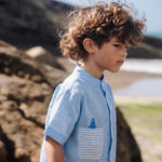 Camisa infantil de linho azul no corpo, bolso listrado e tubarão bordado à mão.