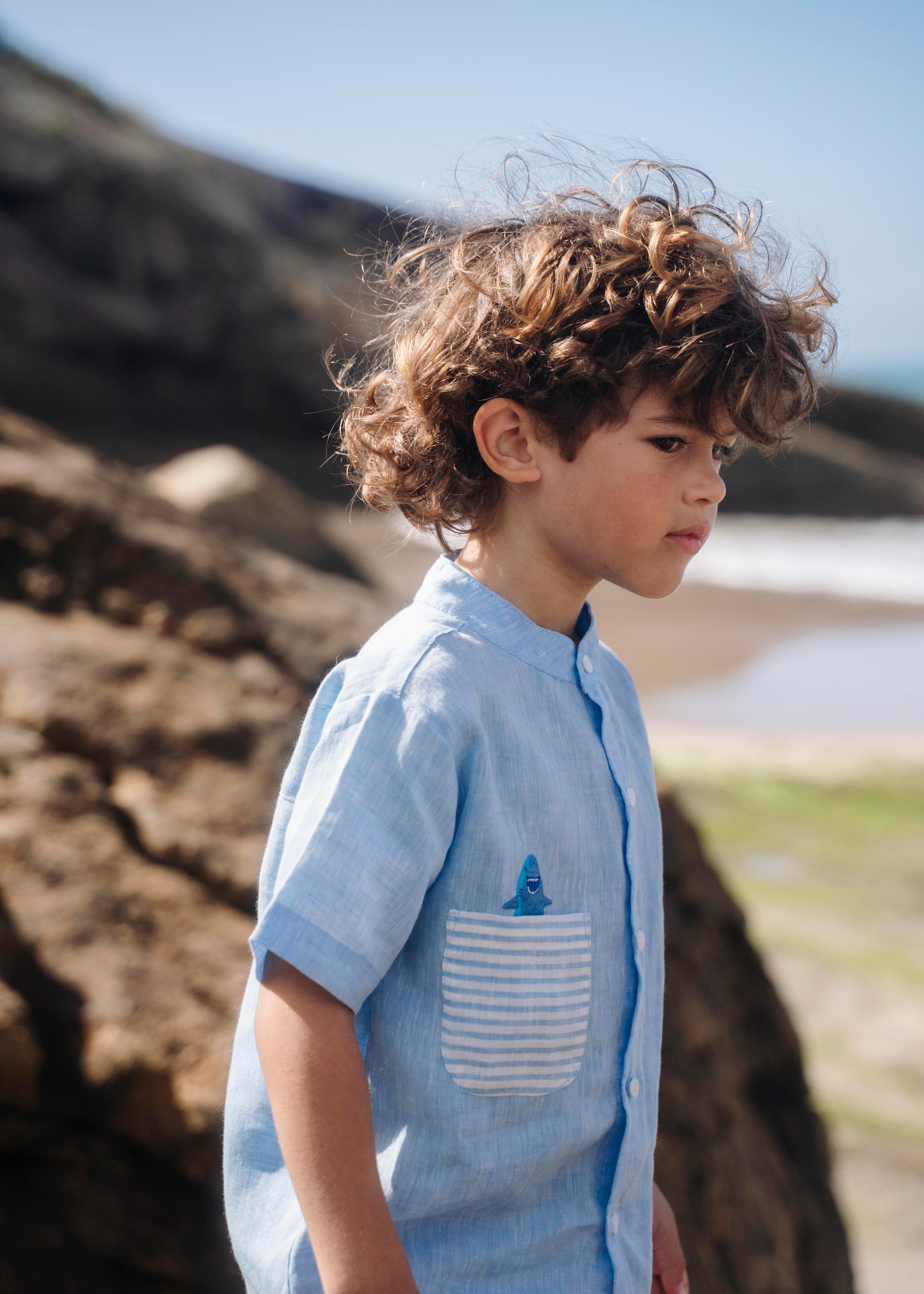 Camisa infantil de linho azul no corpo, bolso listrado e tubarão bordado à mão.