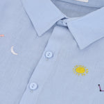 Detalhe do bordado à mão de sol, lua, estrelas e constelação em camisa infantil de puro linho azul claro.
