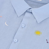 Detalhe do bordado à mão de sol, lua, estrelas e constelação em camisa infantil de puro linho azul claro.