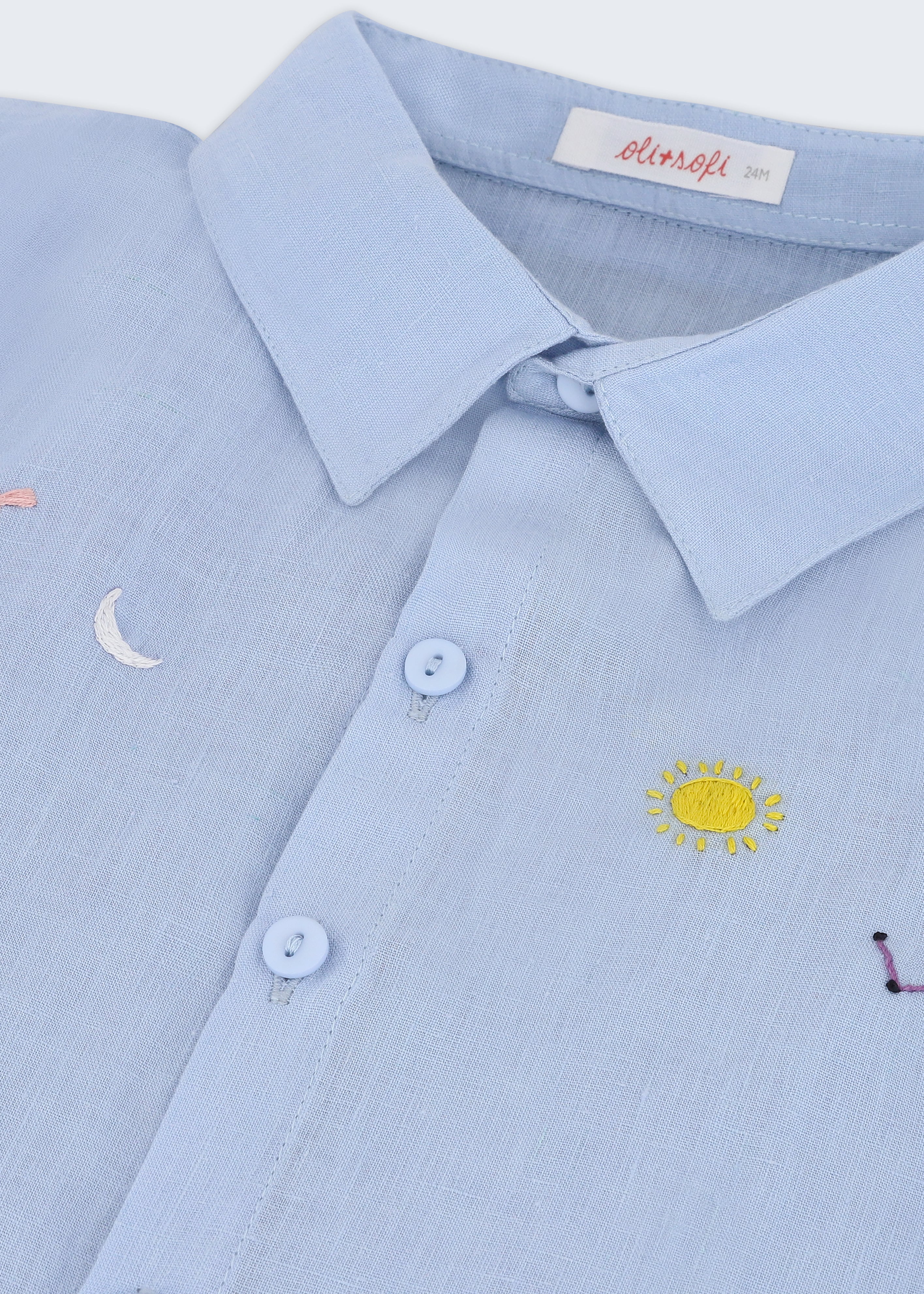 Detalhe do bordado à mão de sol, lua, estrelas e constelação em camisa infantil de puro linho azul claro.