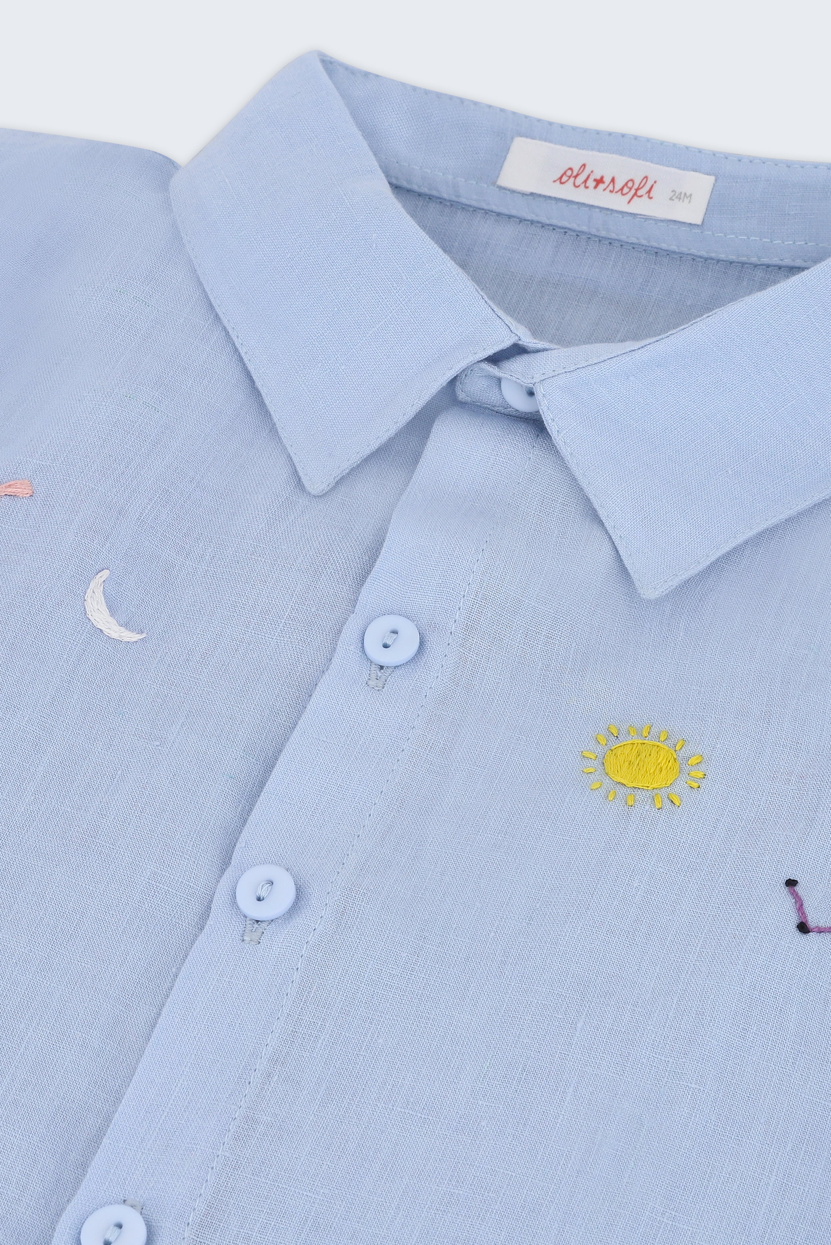 Detalhe do bordado à mão de sol, lua, estrelas e constelação em camisa infantil de puro linho azul claro.