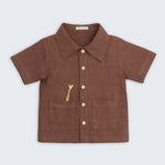 Camisa infantil de menino em linho marrom com bolsos frontais e bordado artesanal de girafa.
