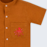 Camisa em linho marrom terracota com polvo bordado no bolso e botões brancos contrastando vista em detalhe.