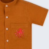 Camisa em linho marrom terracota com polvo bordado no bolso e botões brancos contrastando vista em detalhe.