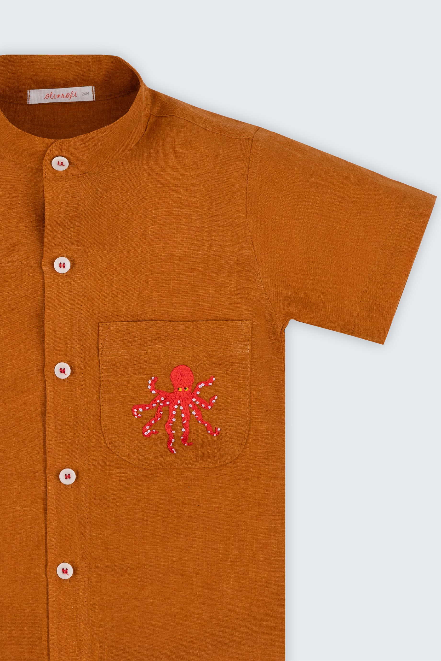 Camisa em linho marrom terracota com polvo bordado no bolso e botões brancos contrastando vista em detalhe.