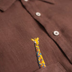 Detalhe do bordado à mão de girafa em camisa infantil de linho marrom para menino.