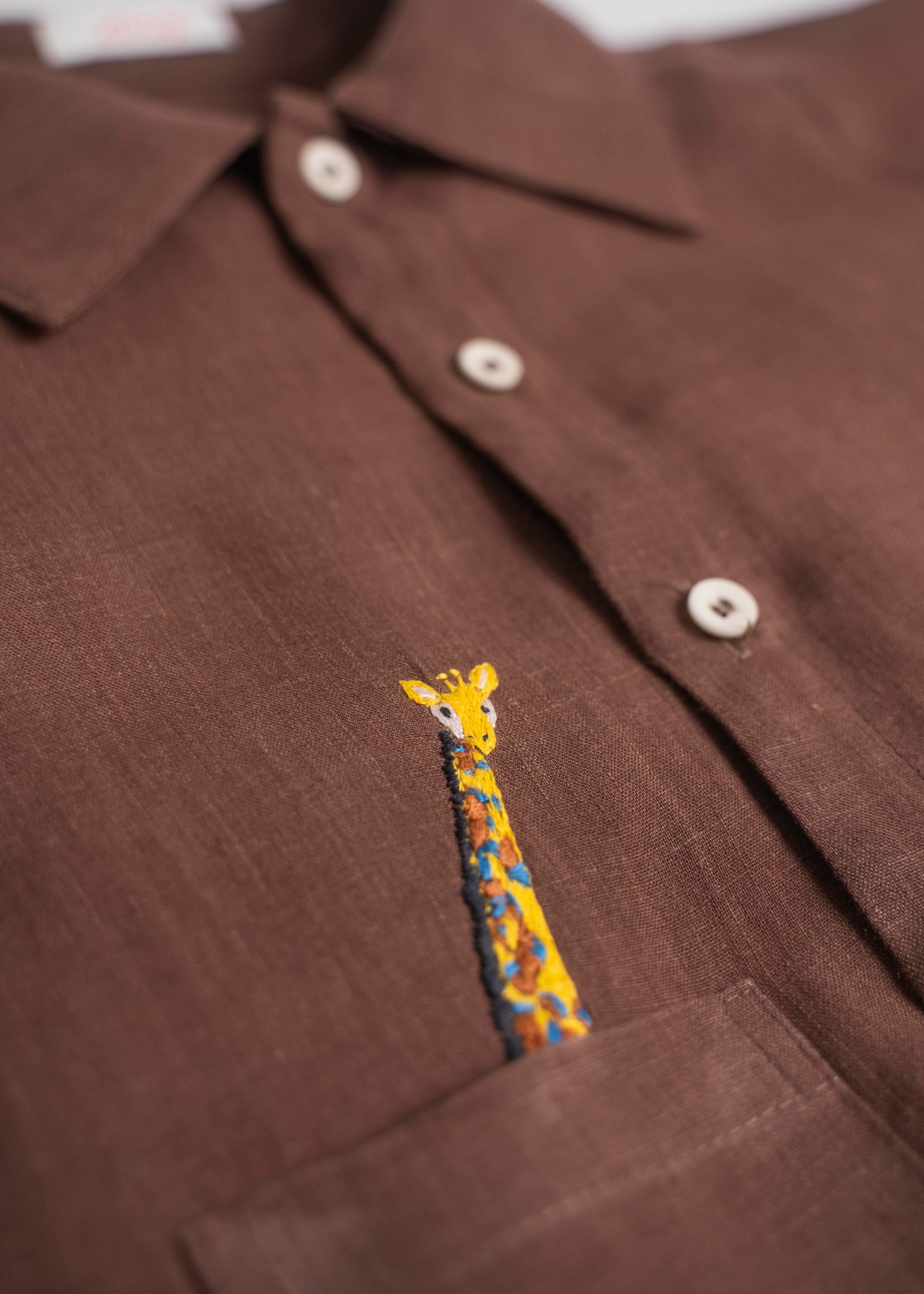 Detalhe do bordado à mão de girafa em camisa infantil de linho marrom para menino.