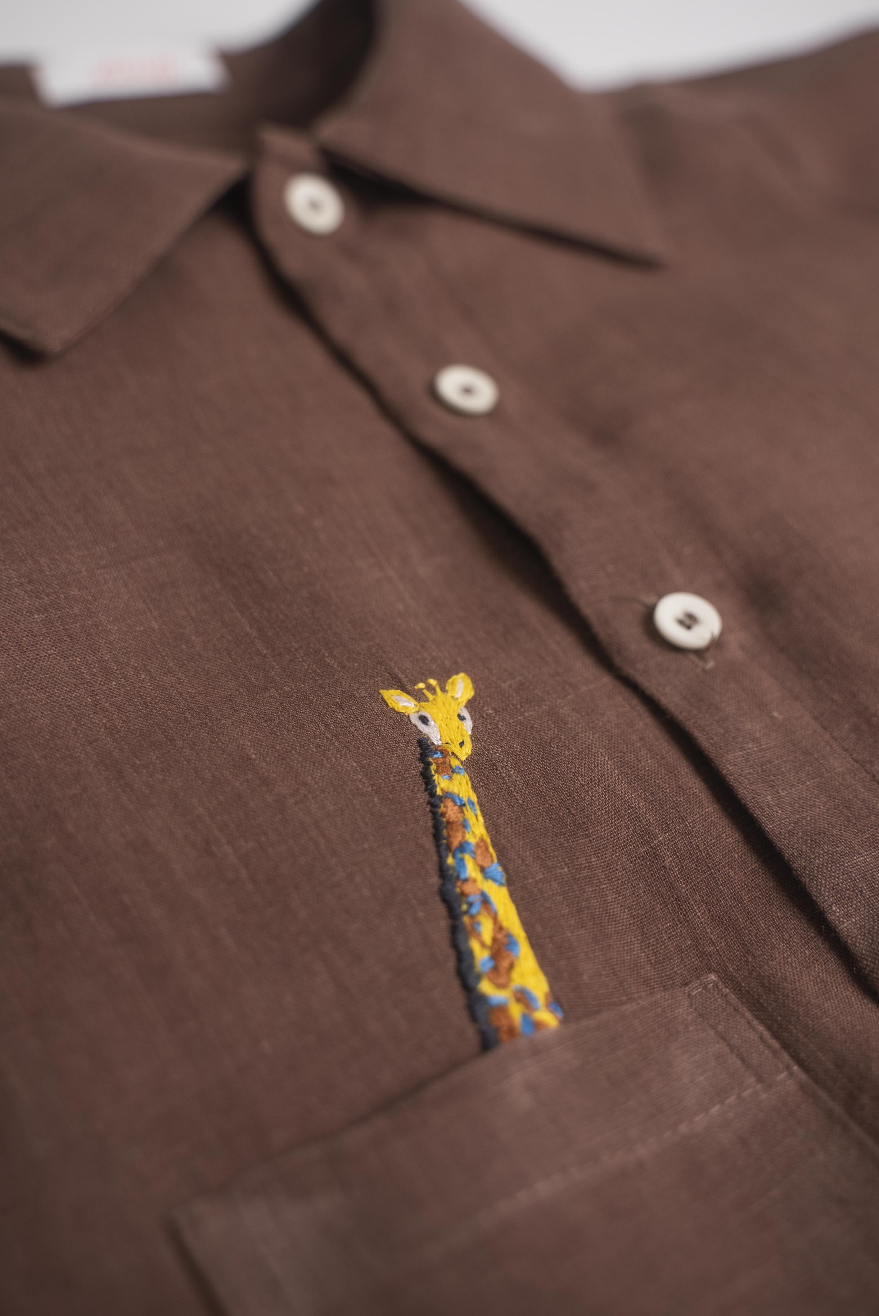 Detalhe do bordado à mão de girafa em camisa infantil de linho marrom para menino.