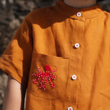 Close de camisa em linho terracota terracota com polvo bordado no bolso e botões brancos contrastando.