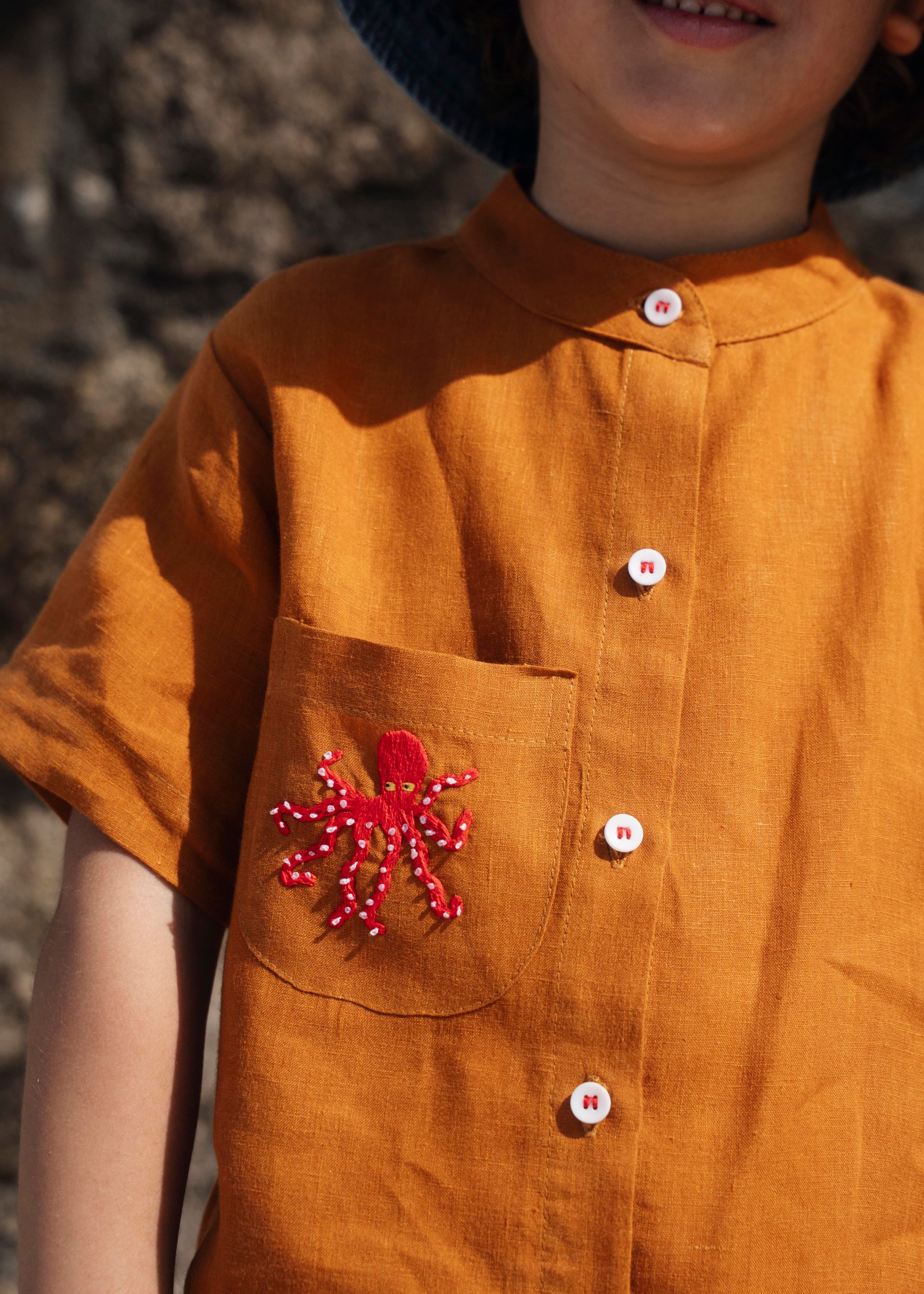 Close de camisa em linho terracota terracota com polvo bordado no bolso e botões brancos contrastando.