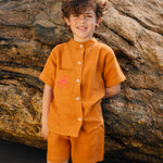 Menino usando camisa infantil em linho puro terracota com gola padre e polvo bordado à mão no bolso.